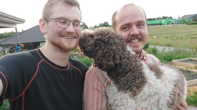 Outdoors selfie of myself, Reynir of Robur workers cooperative, and the family dog. The dog is licking my face