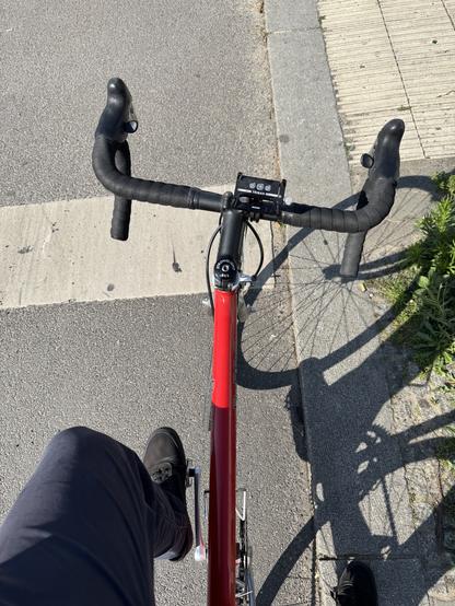 Ein rotes Rennrad steht an einer Kreuzung, das Bild ist aus der Perspektive einer Person aufgenommen, die darauf sitzt.
