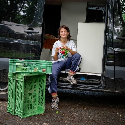 Noa Schärz sitzt in der offenen Türe ihres Vans und hält Radieschen in der Hand.