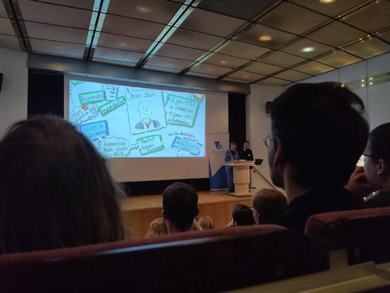 Präsentationsfolie mit Sketch notes zu Jean Stock vor einem Vortragspublikum.