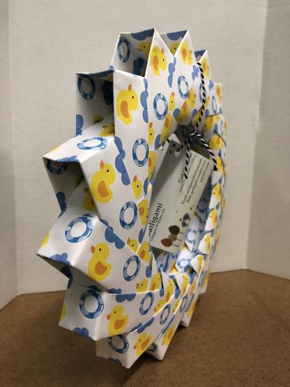 A paper wreath featuring a yellow rubber duck and blue bubble pattern, displayed against a plain background, conveys a playful, cheerful tone.