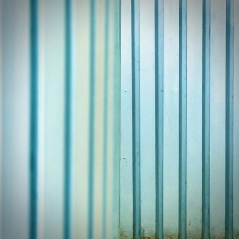 A teal counter wall facade supported by rows of vertical slats remains out of focus on frame left as it wraps around into the distance, becoming in-focus as a perpendicular wall on frame right.