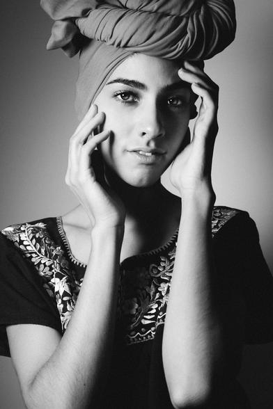portrait of a young Mexican actress and model wearing a head wrap and bun on her head, her hands embracing her face