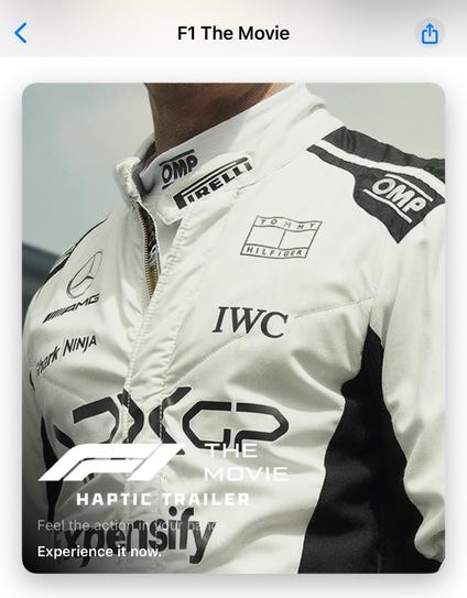 Image of a racing driver's upper torso, wearing a white racing suit with various sponsor logos, including Pirelli and Tommy Hilfiger. The text overlays promote "F1 The Movie" and emphasize a haptic trailer experience.