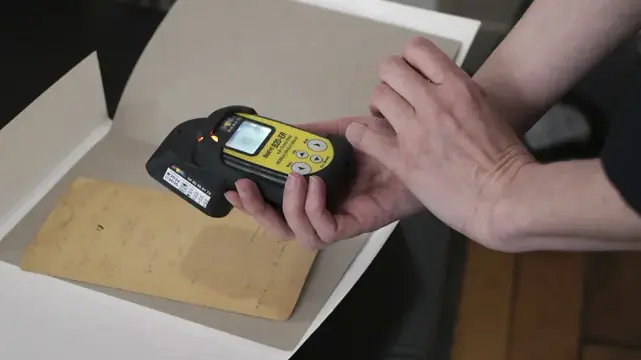A Geiger counter taking a reading from a manuscript in an archival folder.