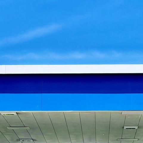 Blue and white gas station canopy against a blue sky with slight wisps of clouds