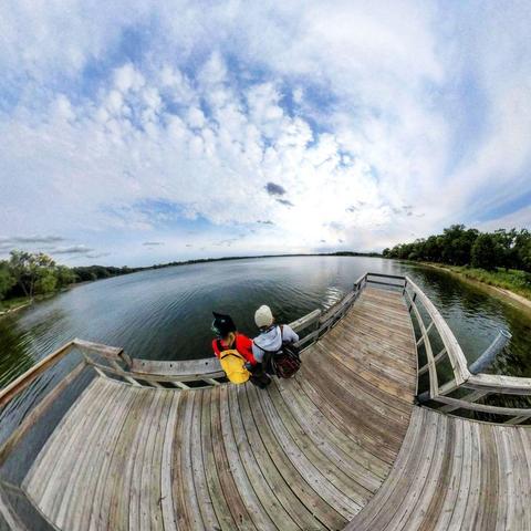 One of a series of photographs in which two people are pictured hiking, biking, and kayaking throughout a beautiful and verdant state park in central Minnesota under cloudy blue late-summer skies.