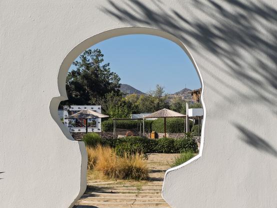 A head-shaped cutout in a wall frames a garden view at Minos Beach Art Hotel in Crete, Greece.