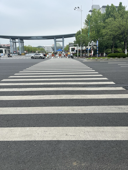 A pedestrian crossing over 6 lanes, looking toward a university campus.