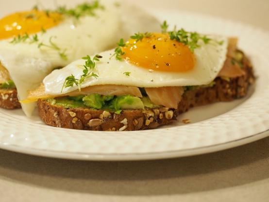 Zwei mit Avocado, Räucherlachs und Spiegelei belegte Brote auf einem Teller. es wurde noch etwas frische Kresse über das Soiegelei gestreut.