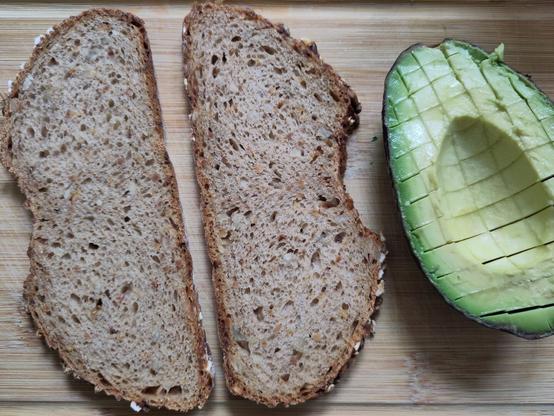 zwei Brotscheiben nehmen einer Avocadohälfte, deren Fruchtfleisch würfelförmig eingeschnitten wurde.