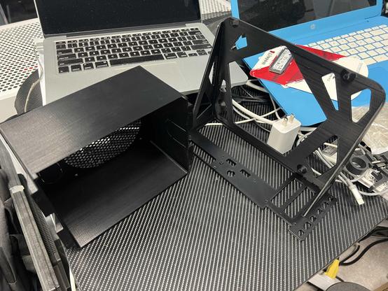 Print of the rear of the hard drive cage and the Mini-ITX motherboard tray sitting on a desk with some other random computer related 'flotsam'