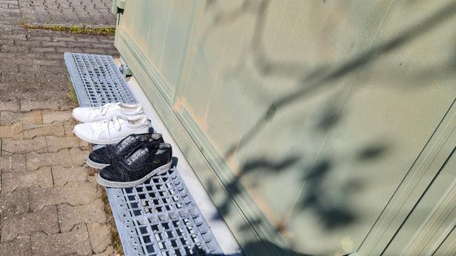 Zwei Paar Schuhe auf Treppenstufen aus metallgitter vor einer metallenen Tür von irgendwas. Schuhe makellos, eins weiss, anderes schwarz, scheints zum verschenken.