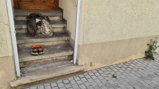 Kleider und ein paar Schuhe liegen auf Steintreppe eines Hauseingangs, die Schuhe schön ordentlich nebeneinander. Seltsam.