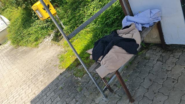 Mehrere Kleider liegen auf sitzbank einer Haltestelle, scheints guter Zustand. Zum mitnehmen?