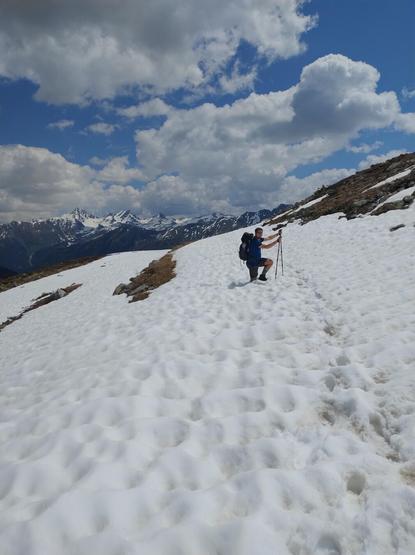 I stand amidst leftovers of a snow field. My right leg sinks into the snow so only half of it can be seen. I smile cheerfully.