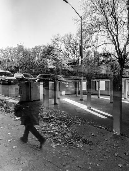 A figure hurrying down a city street reflected on a window of an abandoned storefront