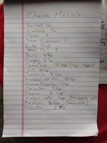a paper notepad page with pencil writing: Chana Masala, followed by a long list of spices and ingredients.