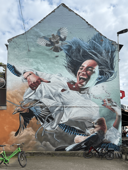 A photo of streetart showing a black haired girl/young woman wearing a white shirt lifting the underside of that shirt. From under the shirt a bird is flying away