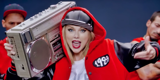 Taylor Swift holding a large 80s boom box with a black baseball cap and red hoodie. “Shake It Off” is an upbeat track that encourages listeners to let go of small problems.