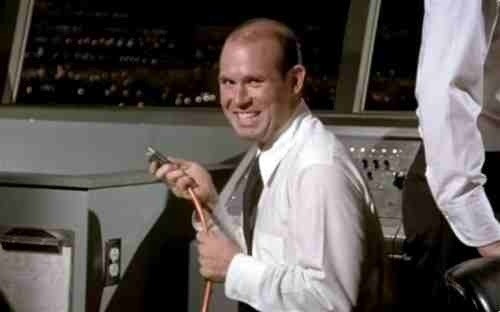 A screenshot from the movie Airplane. A man grins mischievously at the camera while holding an unplugged extension cord.