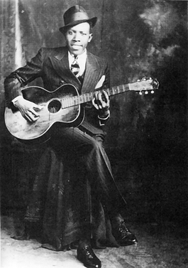 Robert Johnson (fair use, Wikipedia), early blues musician playing guitar, smoke in background, wearing pin stripe suit