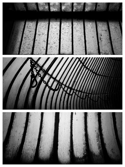 Black and white triptych of photos arranged vertically, depicting opaque and dirty panes of glass set in thin metal frames. The top and bottom photos depict panes running vertically and the middle photo shows panes curving around to the right with a metal chain and hook suspended in loops along the middle of the photo. The mood of all three photos is dark and and sombre