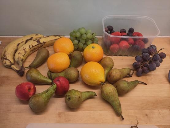 A countertop with a random collection of fruits spread: bananas, pears, nectarines, oranges, grapes, strawberries, etc