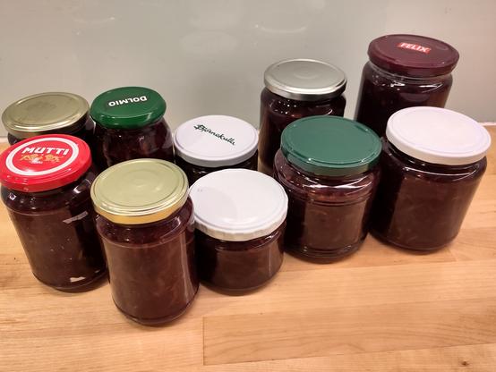 10 varied jars of dark red jam on a countertop