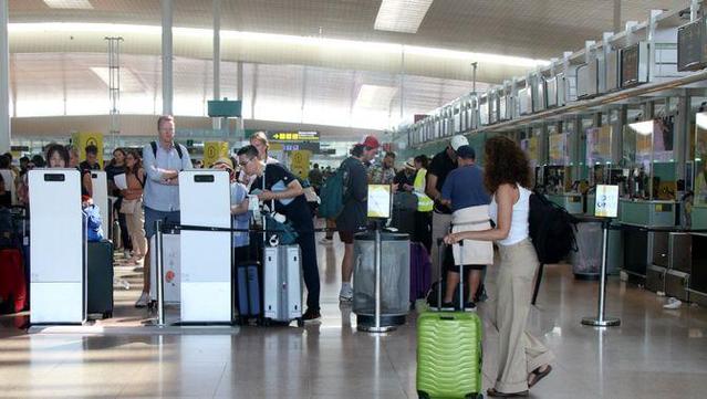 Una noia amb maleta de rodes i motxilla davant passatgers fent autochecking a la T1 de l'aeroport del Prat (ACN/Albert Hernández)