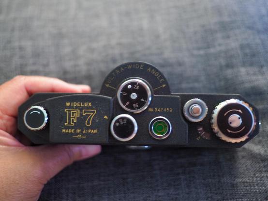 A photo of the top of a vintage film camera with all the dials, being held by a hand.