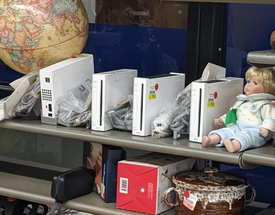 Four nintendo Wii's and an unrelated baby doll sit on a thrift store shelf