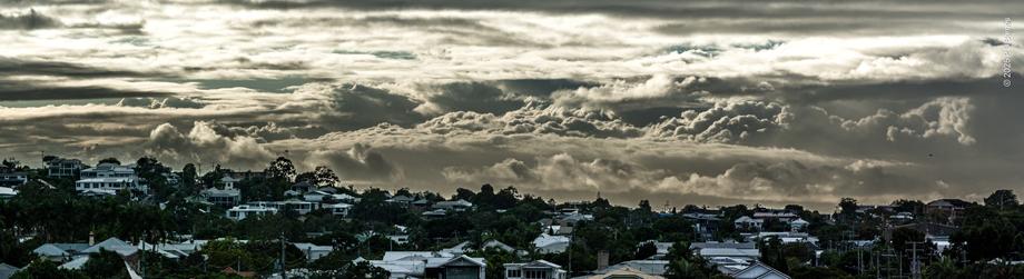 A monochrome suburban skyline surmounted by a dramatic, hectic cloudscape, full of roiling cumulus, deliberately emphasised.