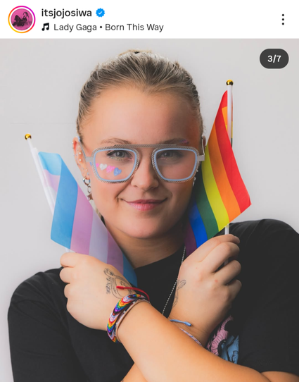JoJo Siwa sosteniendo banderas del orgullo y de la comunidad trans, con una expresión sonriente y un outfit casual.