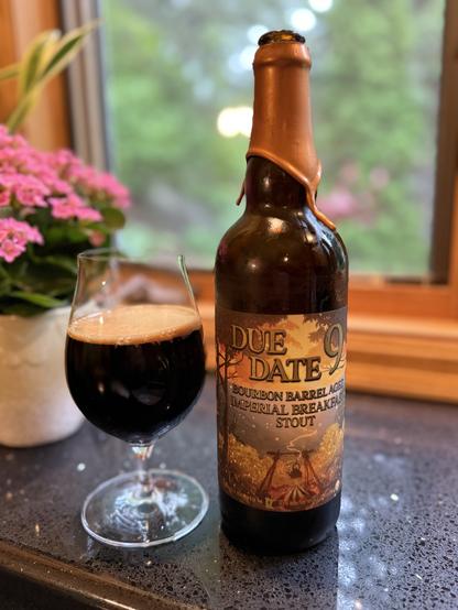 A snifter glass of dark beer is next to a large bottle with a thick wax neck seal and a label in shades of gold and twilight blue