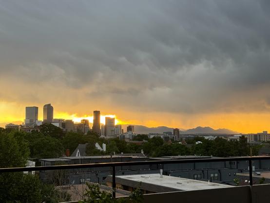 The city skyline silhouetted against the setting sun shining between storm clouds and the mountains.