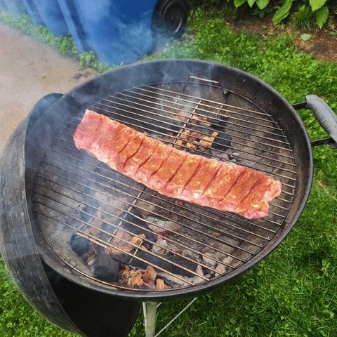 A raw slab of ribs, rubbed with spices, sitting on a grill over smoky coals.