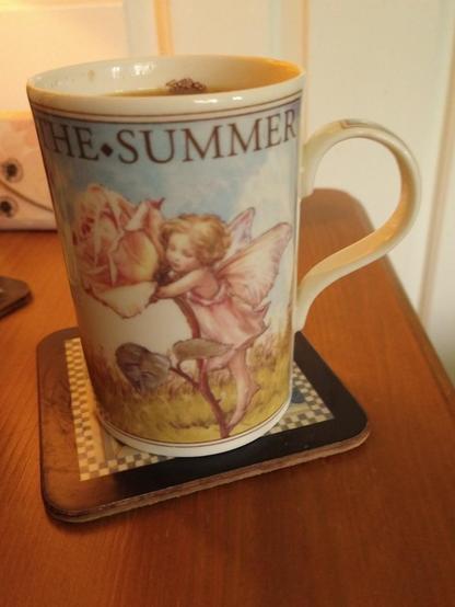 Flower Fairies mug of tea on a bedside cabinet.  The rose fairy and the word summer at the top
