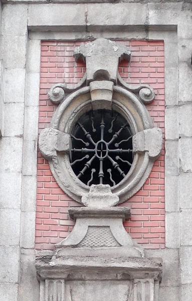 Photo of an oval window with metal decoration that has an oval in the middle surrounded by spikes and what looks like spermatozoa