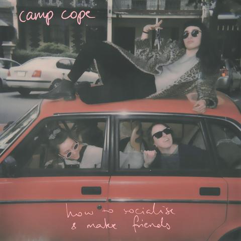 The cover of "How To Socialise & Make Friends" by CAMP COPE features a red Volvo on a Melbourne street, with two band members in the car and one on the roof.