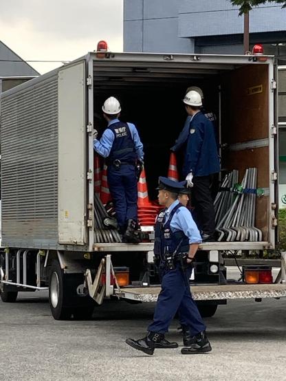 A police vehicle is parked, with officers in uniform unloading traffic cones and equipment from the back. Two officers are loading while another walks by.