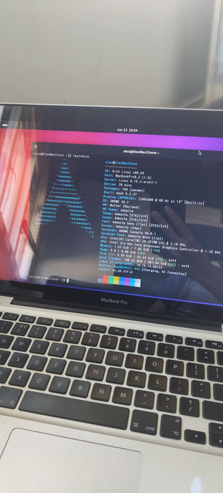picture taken by my phone, of the screen of the macbook. a terminal is on screen with the output of neofetch