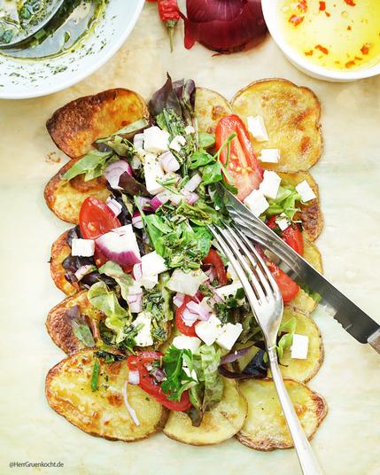 Helles Backpapier. Darauf: Mediterraner Salat mit Feta auf spicy im Backofen gerösteten Kartoffelscheiben mit einer Rosmarin-Estragon Vinaigrette