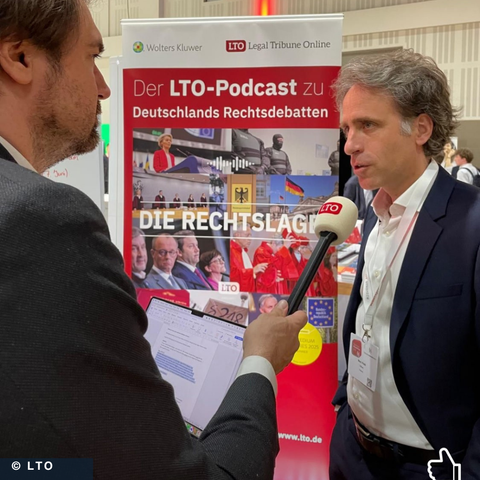 Ein Mann im Anzug wird von einem anderen Mann im Anzug interviewt. Im Hintergrund ein Aufsteller mit dem Text: Der LTO-Podcast zu Deutschlands Rechtsdebatten. Die Rechtslage. Copyright: LTO.