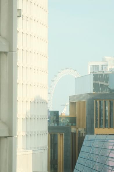Bright and slightly foggy photo of London eye between buildings.