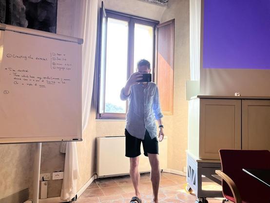 Frank standing in front of an open window, holding his mobile in front of him for taking a photo.
