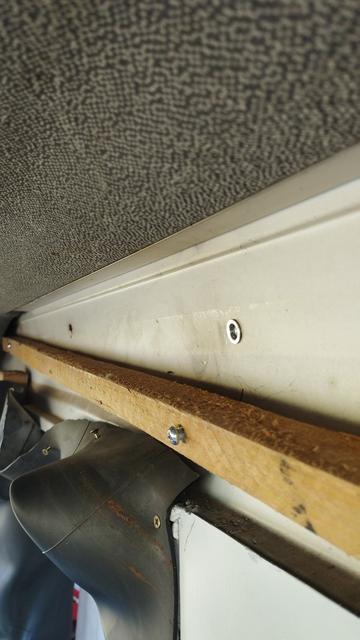 Un insert m6 fixé à la tôle, un tasseau de 23mm de côté pendant en biais en dessous, retenu au bout. Une vis dépasse légèrement en dessous de l'insert dans le bois. La cabine est blanche, le ciel de toit gris moucheté