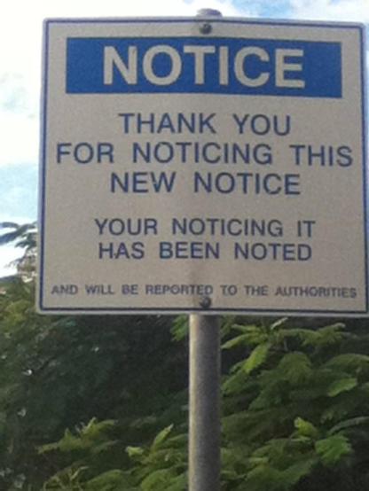 A metal sign on a tall steel-tube post in front of greenery.

White background, blue details:-

NOTICE

THANK YOU FOR NOTICING THIS NEW NOTICE

Your Noticing It Has Been Noted

And will be reported to the authorities