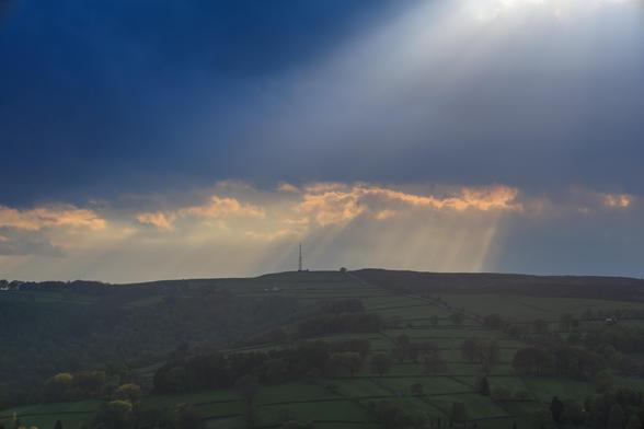 A green ridge line on which sits a large steel radio transmitter - shafts of sunlight shine down from grey clouds