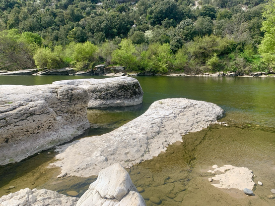 Drei Felsen liegen links in der Ardeche. Ruhiges grünes Wasser und felsiges Ufer der Ardeche auch auf der anderen Flußseite. April 2023